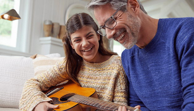 A Medicare recipient in glasses playing guitar with his granddaughter. 