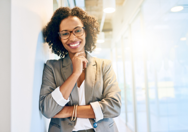 Woman in glasses leans against an office wall.
