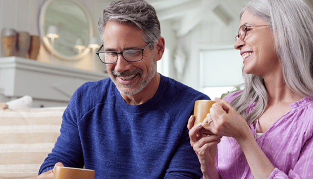 Medicare seniors wearing glasses smiling and having coffee.
