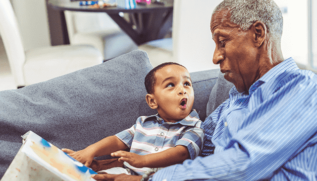 A Medicare recipient grandfather reading a book to his grandson. 